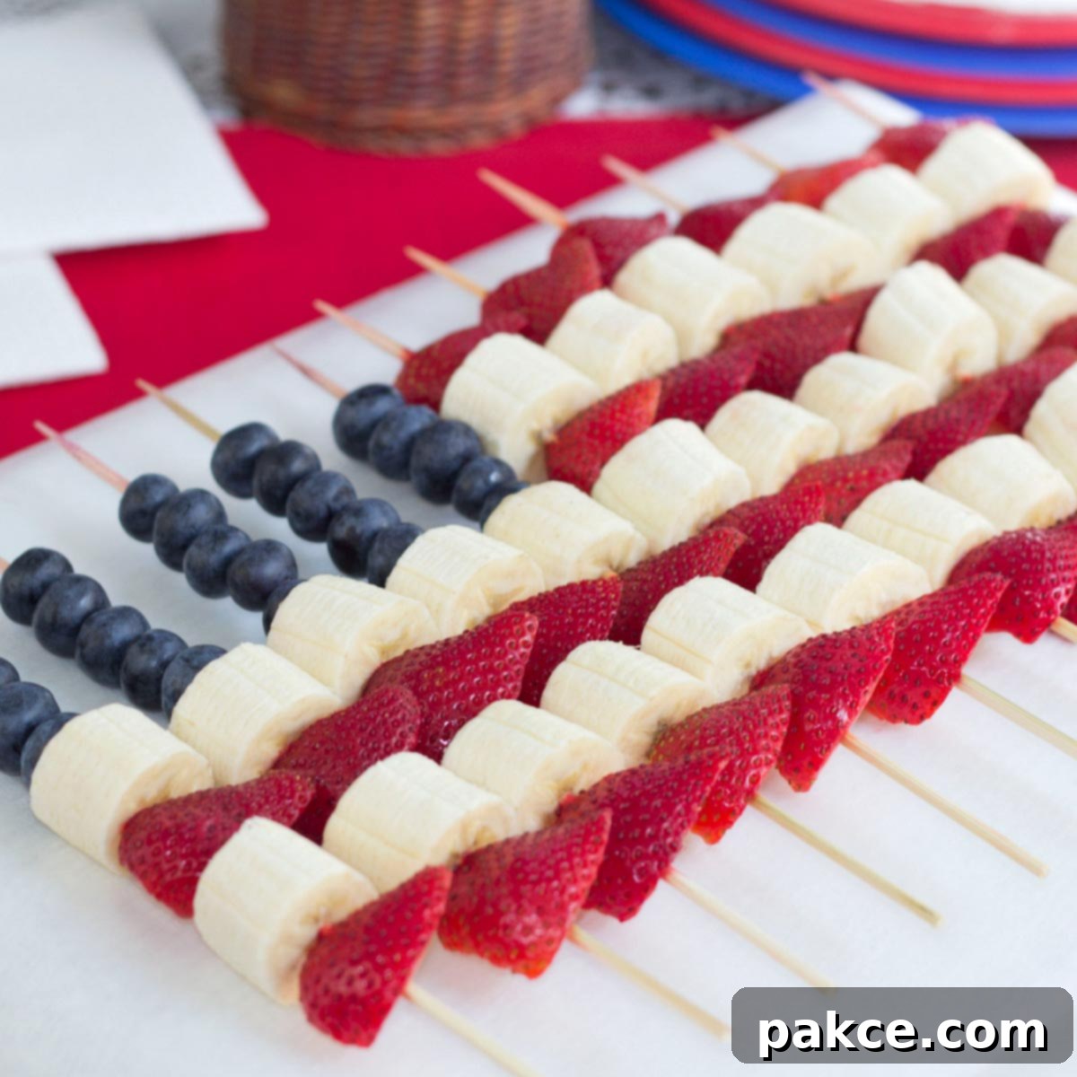 Blueberries, strawberries, and bananas threaded on bamboo skewers in the design of an American flag, showcasing a vibrant red, white, and blue pattern.