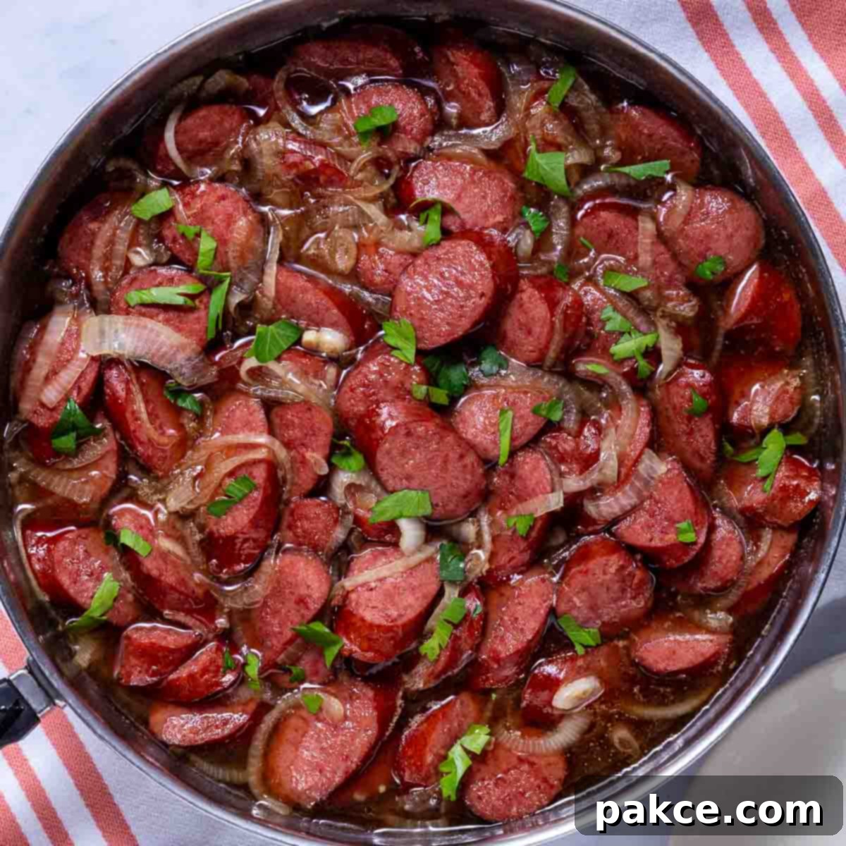 Cooked brown sugar kielbasa in a skillet, glistening with a rich glaze and scattered with caramelized onions.