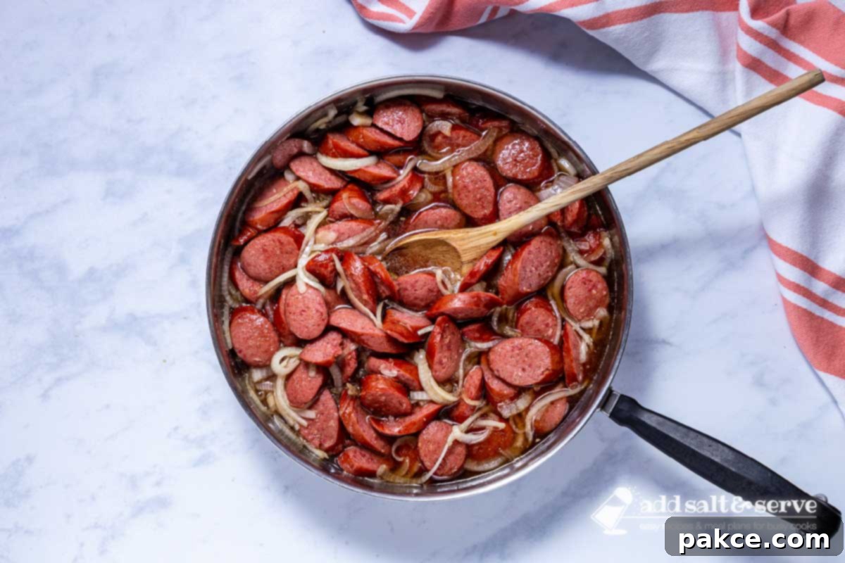 Brown Sugar Kielbasa Skillet 6 A skillet with cooked Brown Sugar Kielbasa, thick and glossy with glaze, ready to serve, with a wooden spoon resting inside.