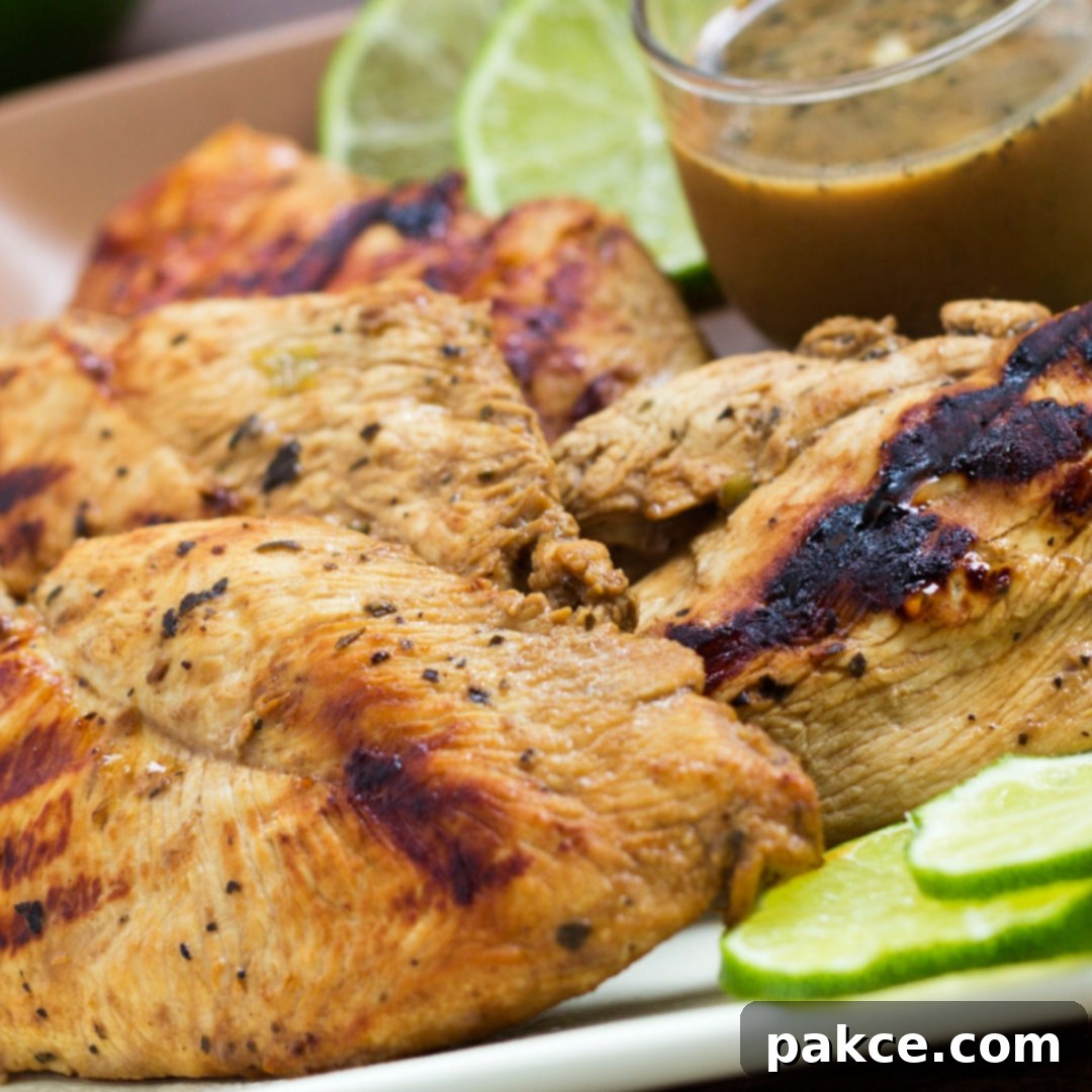 Grilled chicken on a square plate, garnished with lime slices. A small clear glass cup of Dijon basil lime dipping sauce is on the plate.