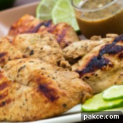 Zesty Basil Lime Chicken 3 Grilled chicken on a square plate, garnished with lime slices. A small clear glass cup of Dijon basil lime dipping sauce is on the plate.