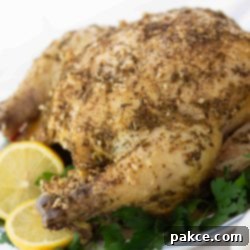 Easy Greek Chicken Crockpot or Air Fryer 2 Whole roasted chicken with a dried rosemary and minced garlic rub on a white plate, garnished with lemon slices and parsley.