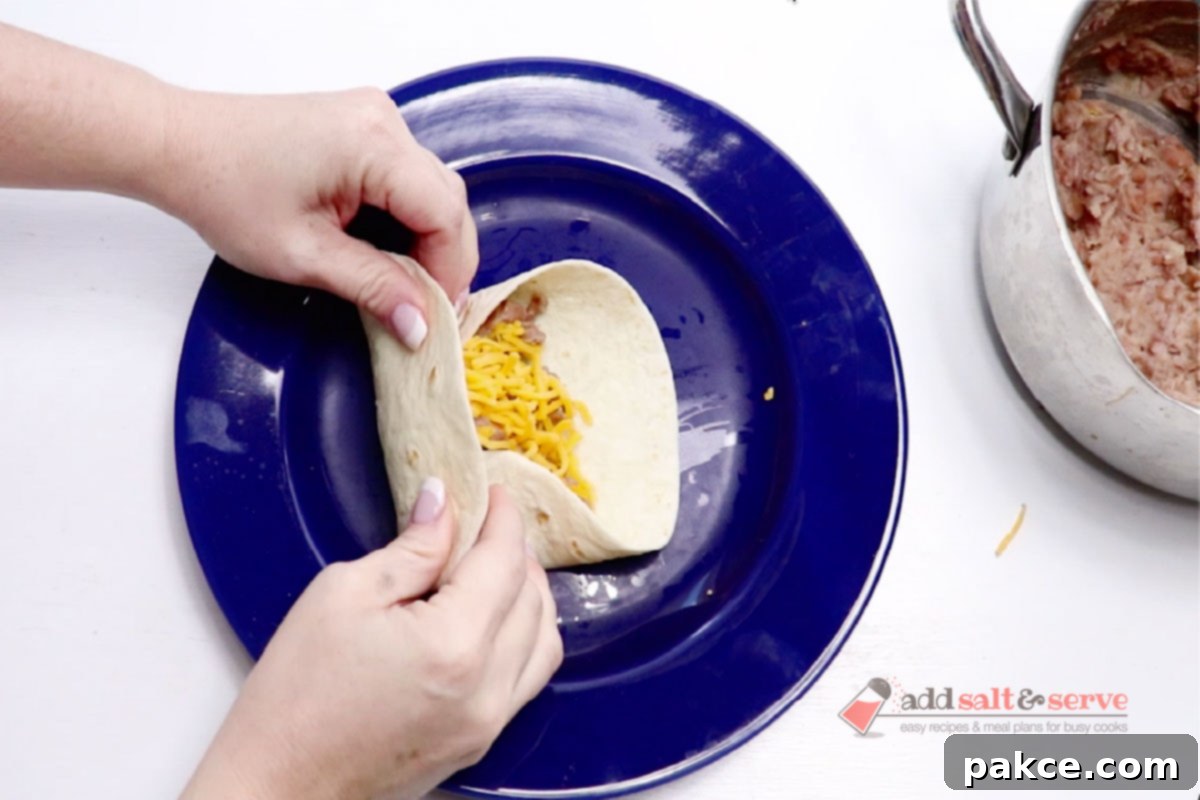 Classic Smothered Burritos 9 A warm flour tortilla with bean and cheese filling being expertly folded into a compact burrito shape.