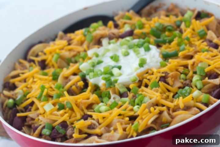 Kidney beans, ground beef, and egg noodles topped with shredded cheddar cheese, sour cream, and chopped green onions, in a skillet. A delicious and easy Southwestern-style one-pan meal.