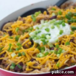 Fiesta Ground Beef Skillet 2 Kidney beans, ground beef, and egg noodles topped with shredded cheddar cheese, sour cream, and chopped green onions, in a skillet. A vibrant and easy Southwestern-style one-pan dish.