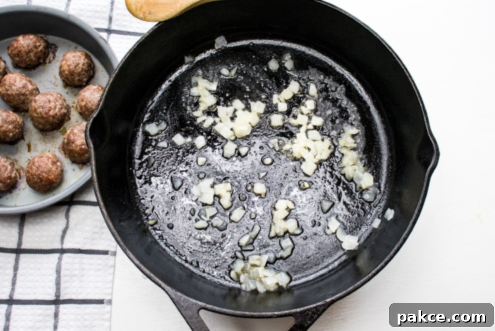 Browning meatballs and sauteing onion Cast iron skillet with chopped onion sautéing and meatballs in a round baking pan to the side