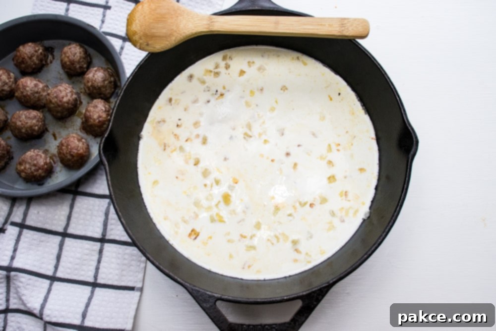 Cream and balsamic simmering for sauce Cast iron skillet with sautéed chopped onion simmering in cream and meatballs in a round baking pan to the side