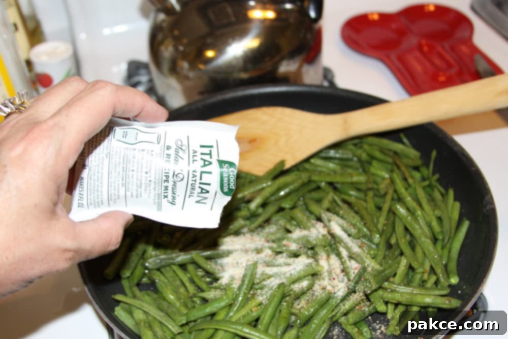 Green Beans Seasoned with Italian Dressing Sautéed green beans in a black fry pan with Good Seasons Italian dressing mix being added