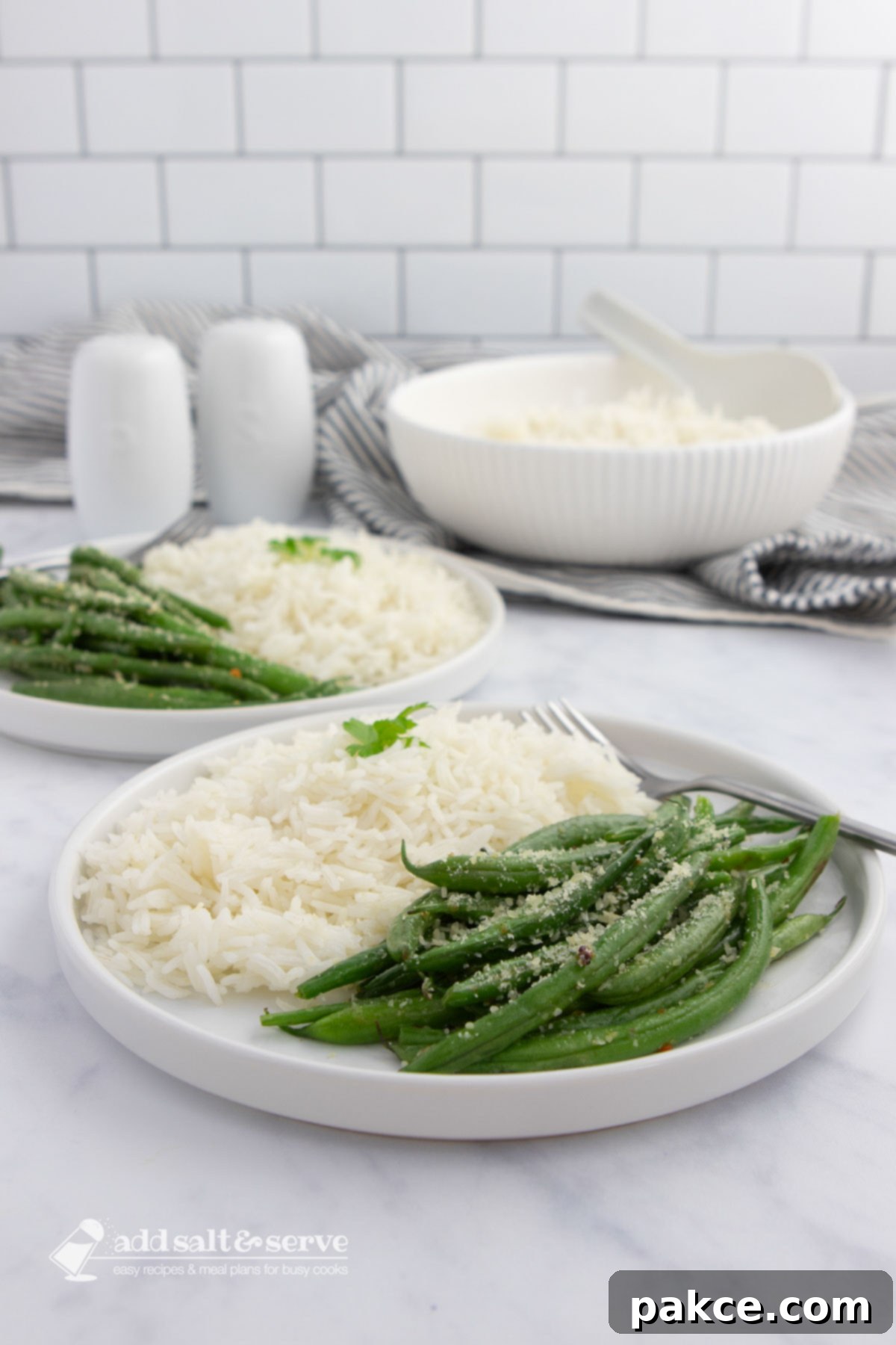 Flavorful Green Beans 3 Seasoned green beans garnished with Parmesan cheese on plates with white rice with a serving bowl of rice in the background.