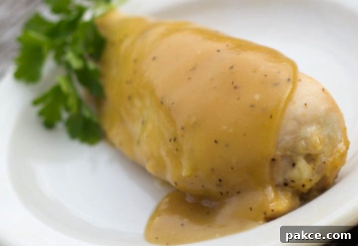 White plate with chicken breast topped with a Dijon sauce.