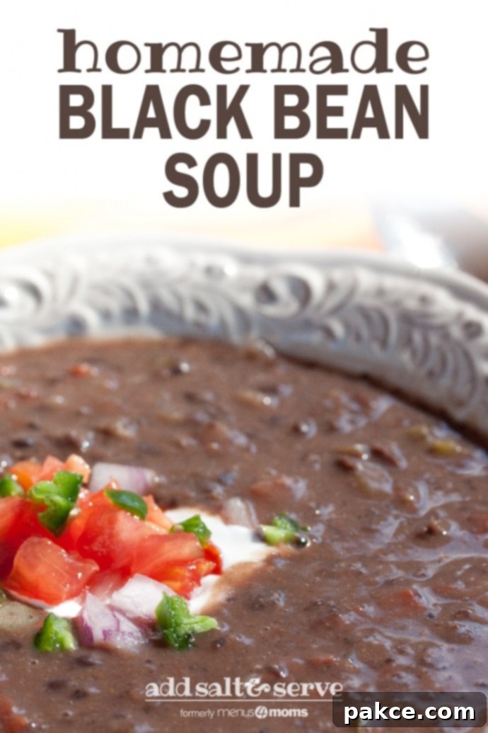 A white shallow bowl with Black Bean Soup garnished with sour cream, diced tomatoes, diced red onion, and fresh cilantro and text Black Bean Soup add salt & serve formerly Menus4Moms