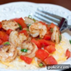 Southern Shrimp and Grits 2 Shrimp, diced tomatoes, and shredded cheddar cheese on grits, on a white plate with a fork.