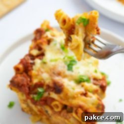 Classic Cheesy Meatless Baked Ziti 11 Forkful of Cheesy Meatless Baked Ziti garnished with fresh parsley held above a serving of the ziti on a plate.