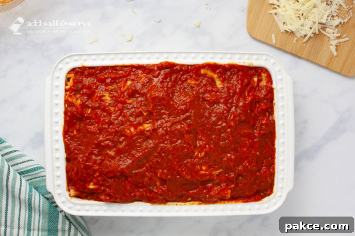 Classic Cheesy Meatless Baked Ziti 6 Pan showing a layer of marinara sauce spread over other layers of baked ziti.