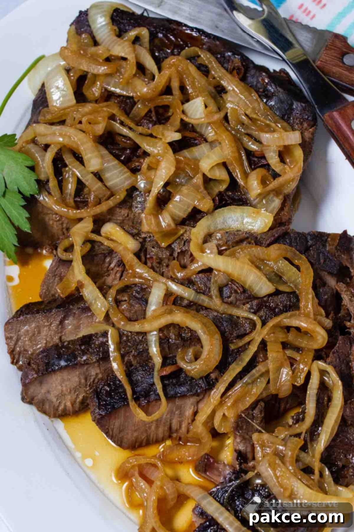 Sliced crock pot London Broil with au jus topped with tender onions and fresh parsley garnish.