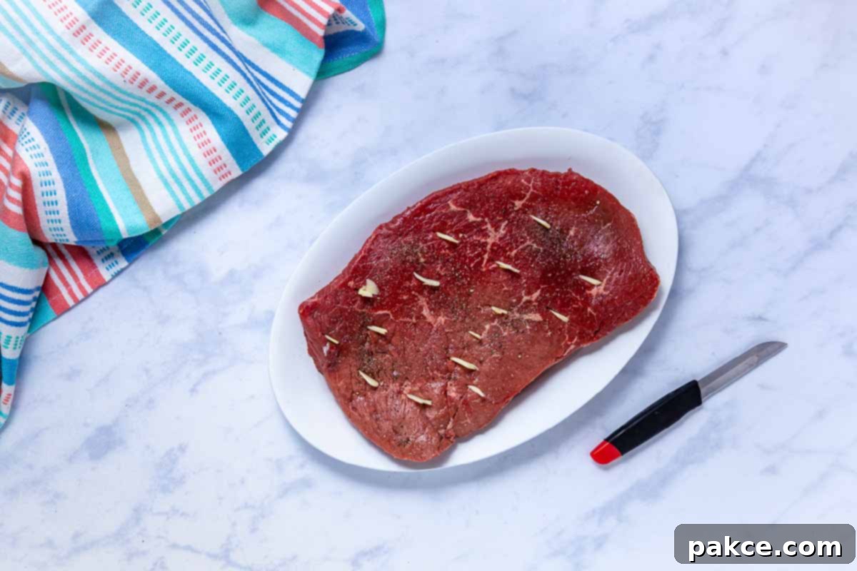 Tender Crockpot London Broil Au Jus 5 Uncooked London broil roast seasoned with salt and pepper with sliced garlic inserted into small slits cut into the roast surface.