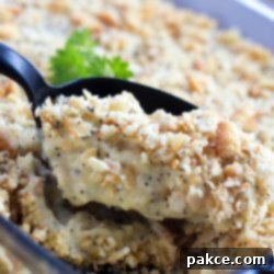Creamy Poppy Seed Chicken Bake 2 A black spoon is scooping Poppy Seed Chicken Casserole out of a clear glass casserole dish.