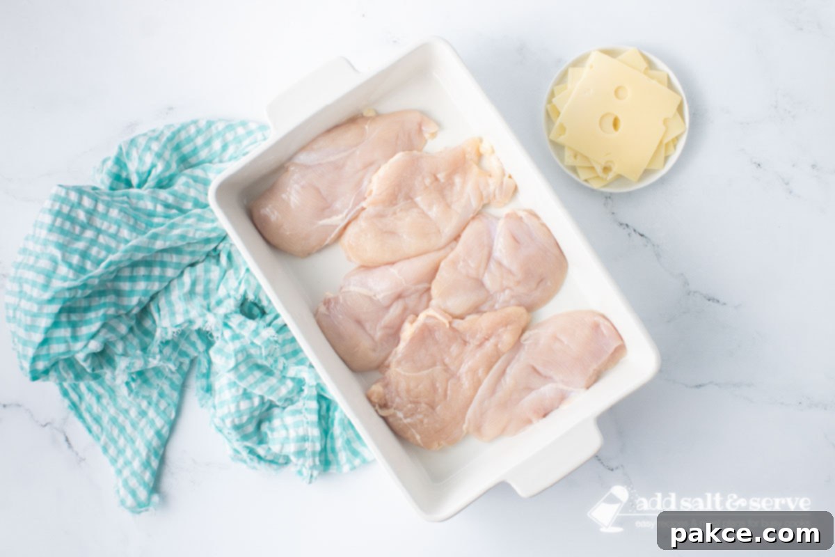 Baked Swiss Chicken with White Wine 4 Casserole dish with chicken breasts and a plate with slices of Swiss cheese to the side.
