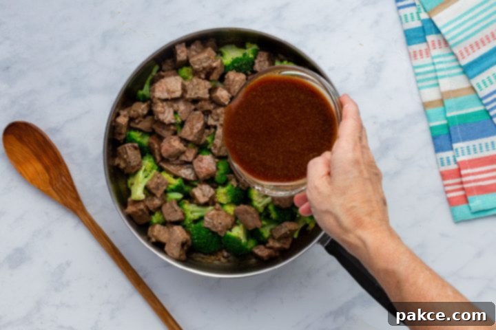 Leftover Steak Beef and Broccoli Makeover 5 Ginger-soy sauce being poured over leftover steak and broccoli in a hot skillet, ready to thicken.