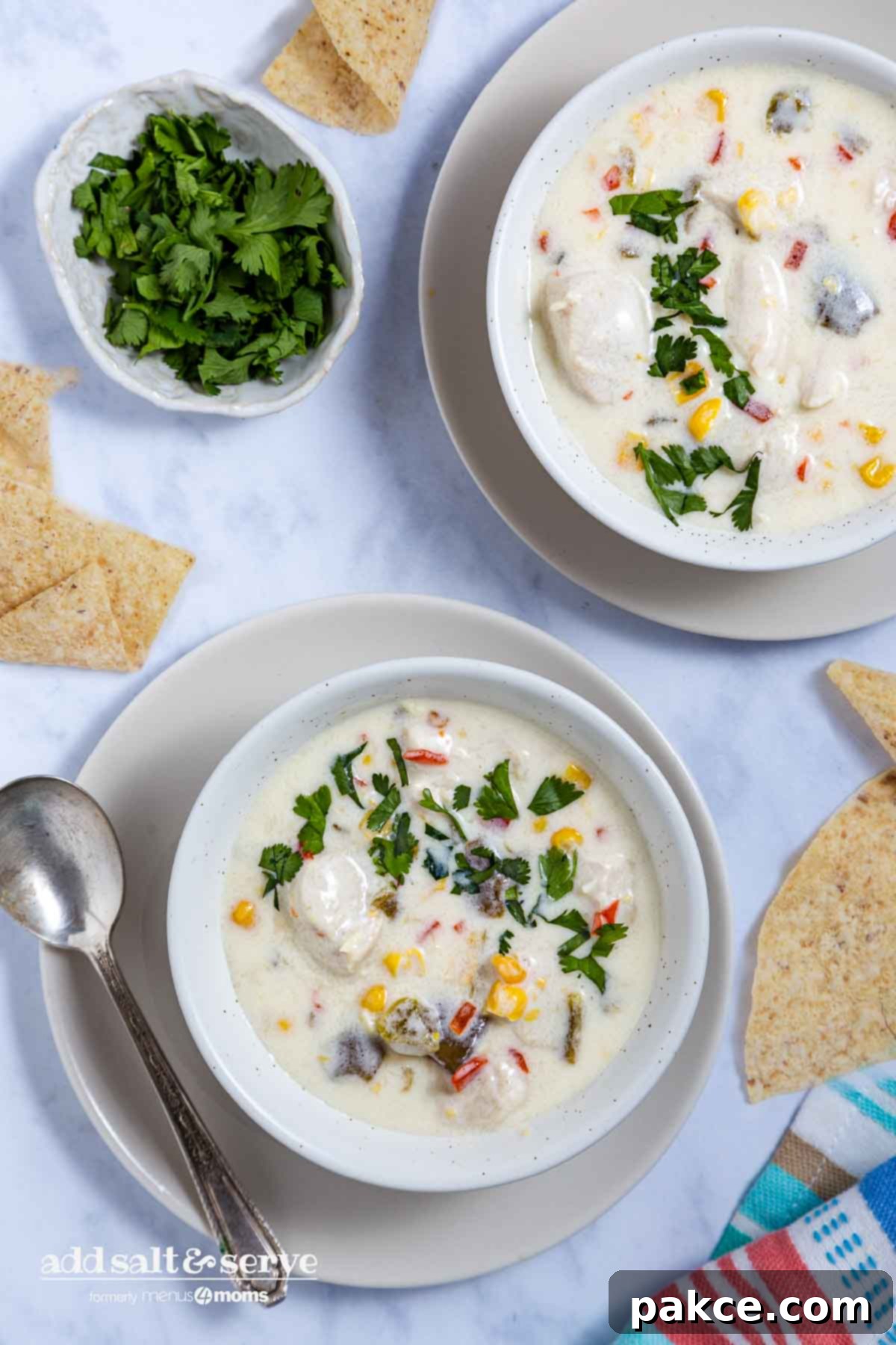 Two bowls of creamy Southwest Chicken Corn Chowder garnished with fresh cilantro and tortilla chips on saucers, ready to be served.