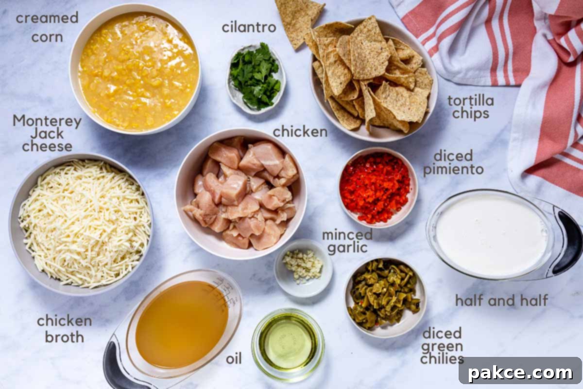 Homestyle Tex-Mex Chicken Corn Chowder 2 A flat lay image showing all the ingredients for Southwest Chicken Corn Chowder: chopped cooked chicken, shredded Monterey Jack cheese, canned creamed corn, minced fresh garlic, chicken broth, diced green chilies, diced pimento, vegetable oil, half and half, fresh cilantro, and a side of tortilla chips for garnish.