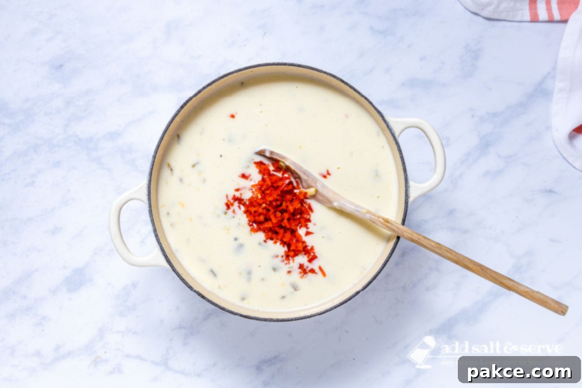 Homestyle Tex-Mex Chicken Corn Chowder 7 Enameled Dutch oven with Southwest Chicken Corn Chowder being stirred with a wooden spoon after all ingredients, including pimientos, have been added and cheese is melted.
