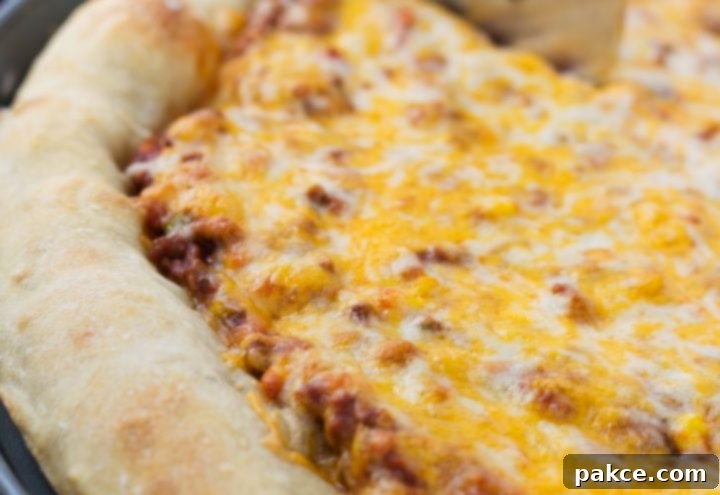Side view of a whole pizza with sloppy joe sauce covered with colby-jack cheese on a thick crust
