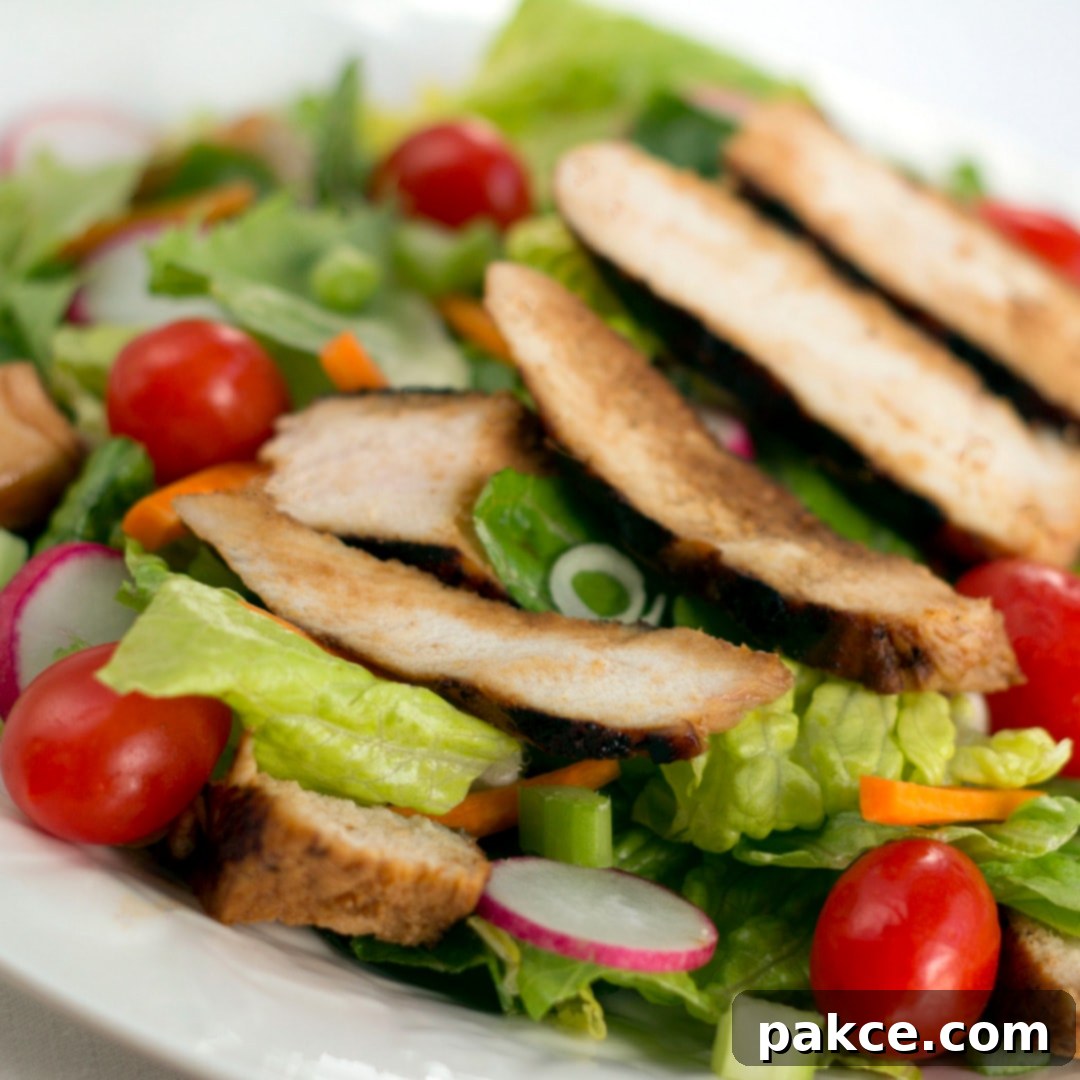 Salad of romaine lettuce pieces, grape tomatoes, and carrots topped with sliced grilled chicken