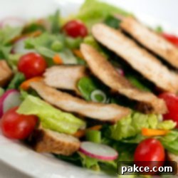 Salad of romaine lettuce pieces, grape tomatoes, and carrots topped with sliced grilled chicken