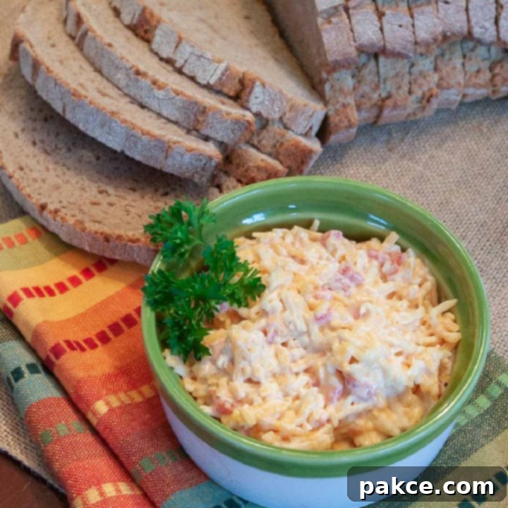 Homemade Pimento Cheese in a green and white bowl, garnished with a sprig of parsley. There is an unpackaged loaf of sliced bread at the top of the photo.