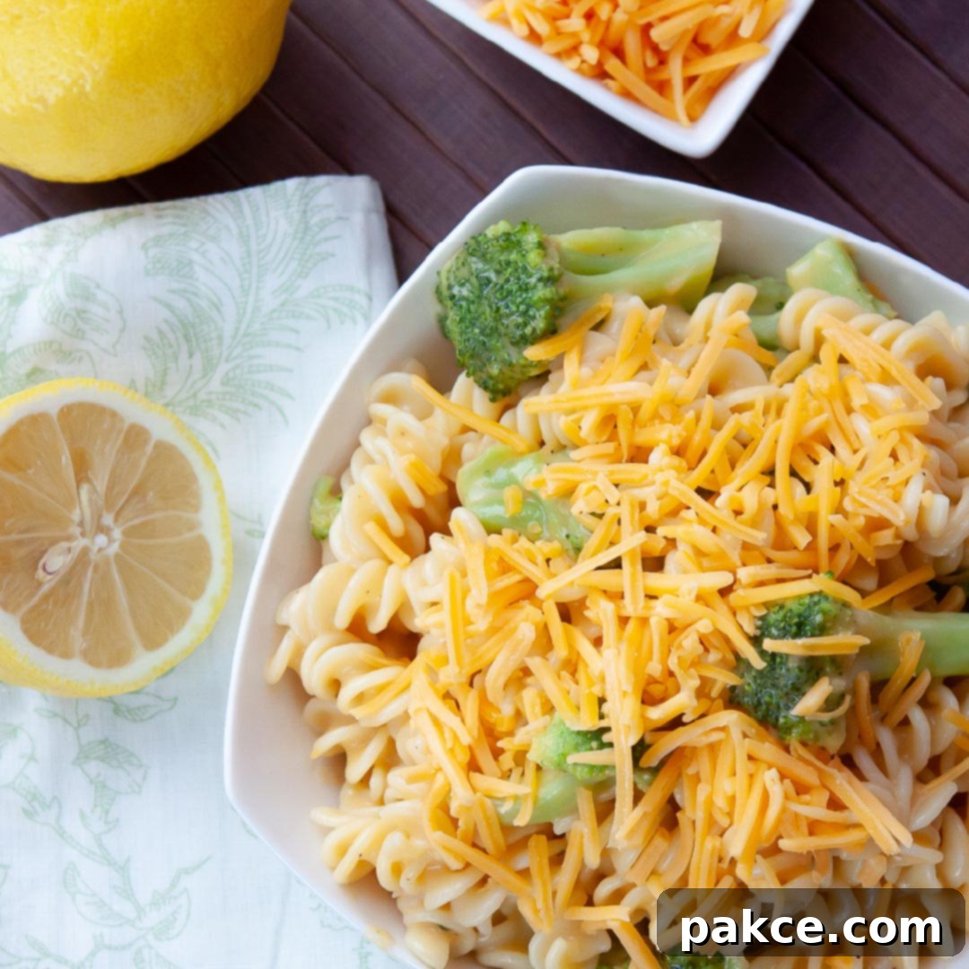 A comforting bowl of Cheesy Spirals with fresh broccoli florets, garnished with extra shredded cheddar cheese, alongside bright lemons and a bowl of additional cheese, ready to be served as a quick, satisfying meal.
