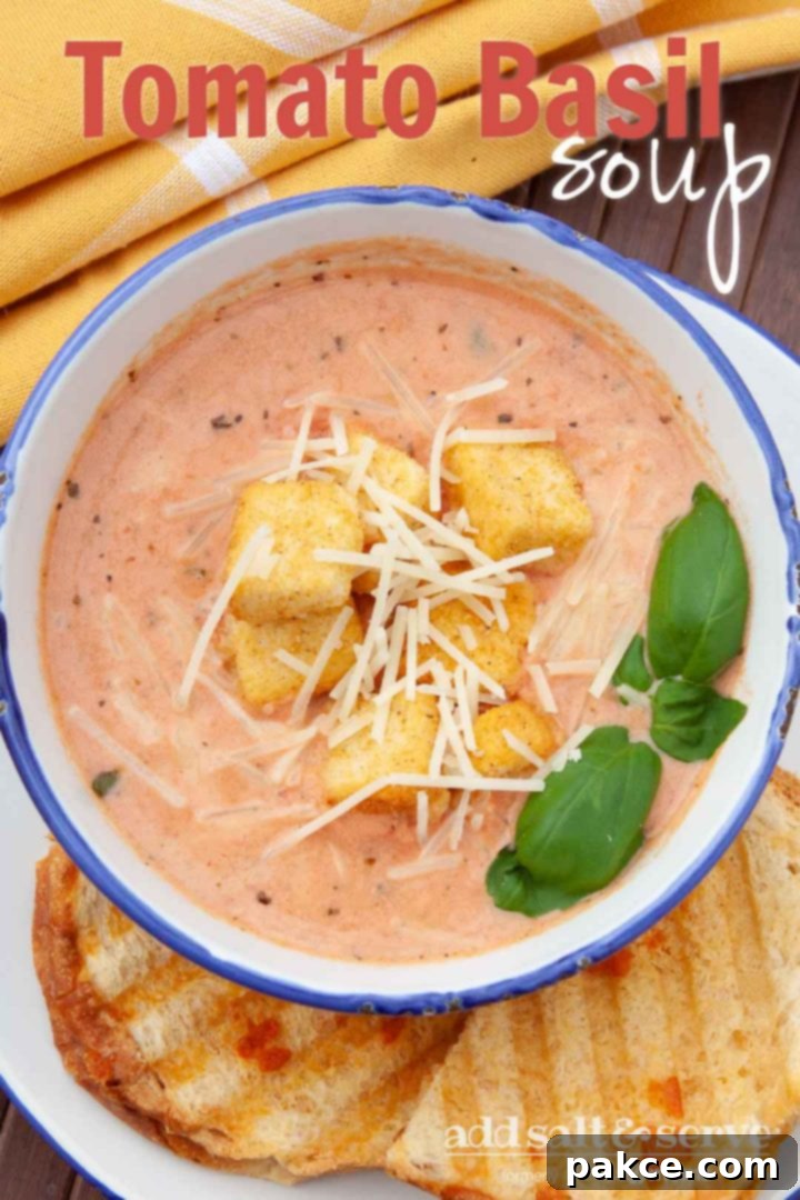 Creamy Tomato Basil Soup in a white and blue bowl, topped with croutons and shredded parmesan cheese. The bowl is on a plate with two slices of garlic bread. Text Tomato Basil Soup Add Salt & Serve formerly Menus4Moms
