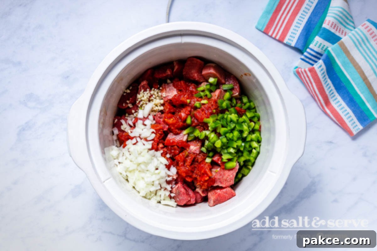 Effortless Slow Cooker Carne Guisada 5 Overhead view of beef, onions, garlic, tomatoes, and bell peppers for Carne Guisada in a crock pot.