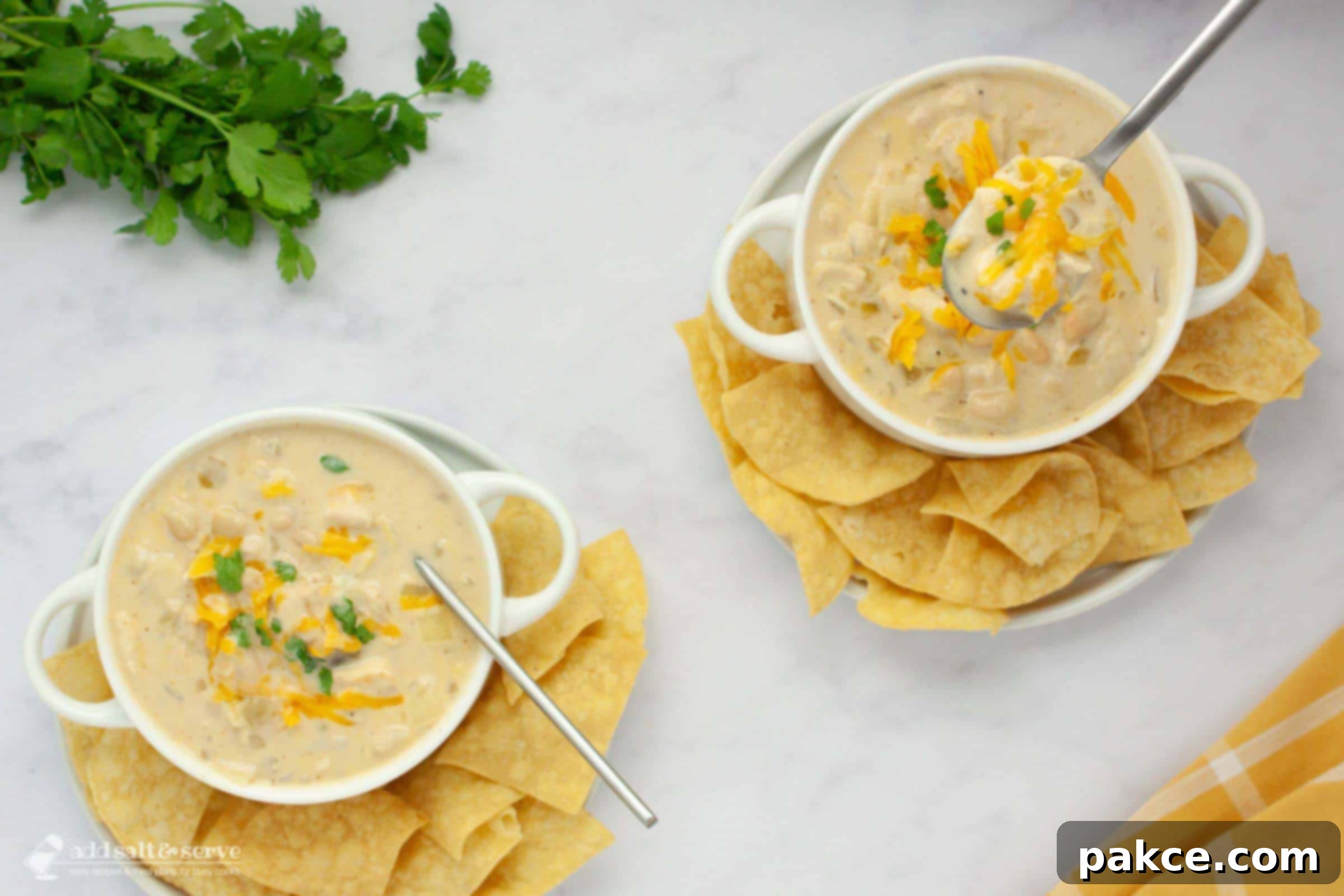 Two bowls of creamy white chicken chili garnished with cheddar cheese and cilantro and served with chips.