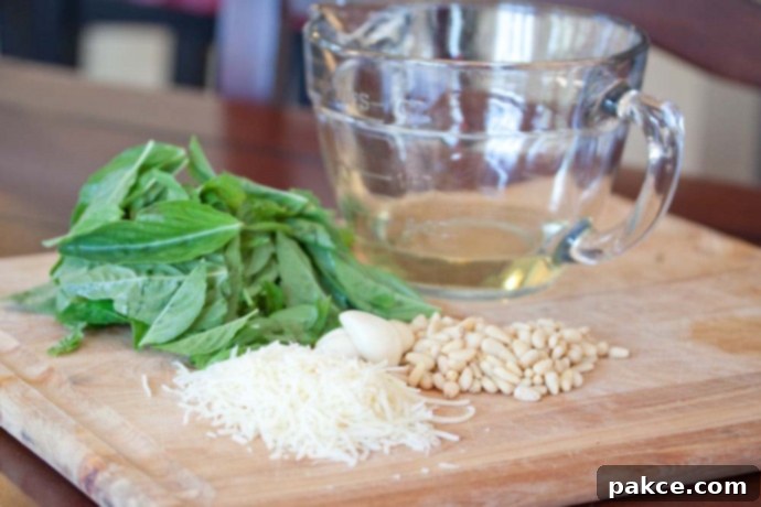 Gathering Your Ingredients for the Perfect Pesto A wooden cutting board showcasing all the fresh ingredients needed for homemade pesto: vibrant basil leaves, whole garlic cloves, golden pine nuts, a mound of shredded Parmesan cheese, and a clear measuring cup filled with olive oil.