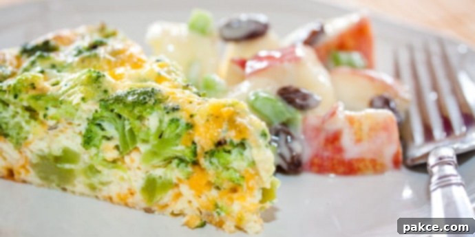 Slice of broccoli and cheese quiche on a plate with apple and raisin salad on a white plate with a fork.
