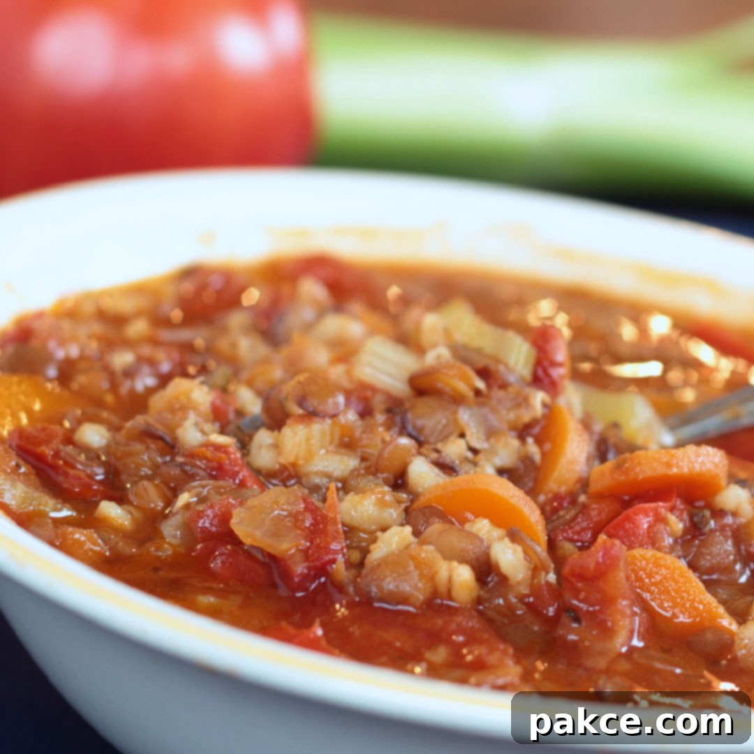 A comforting bowl of hearty barley lentil soup, brimming with wholesome ingredients like tender barley, nourishing lentils, sweet carrots, rich tomatoes, and a savory broth, served in a classic white bowl.