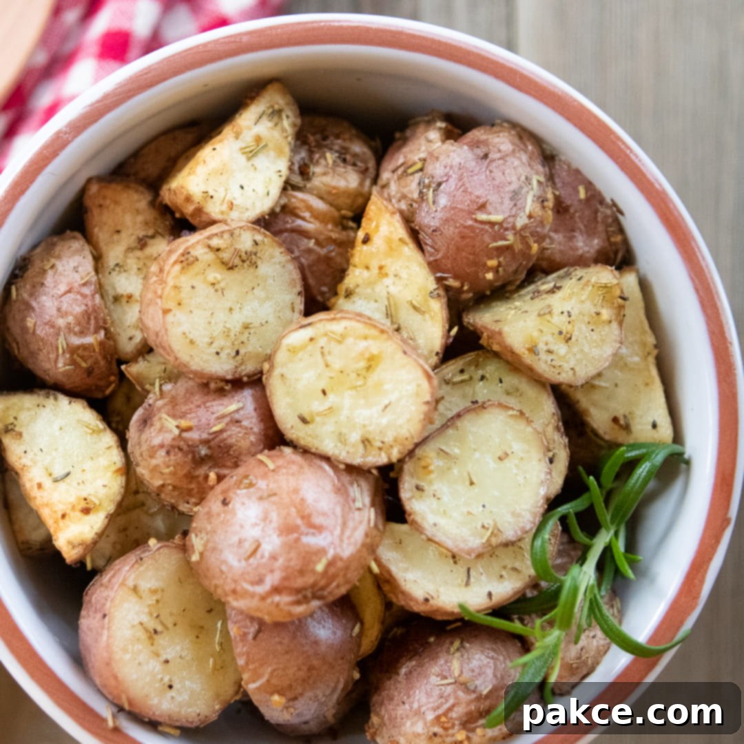 Bowl of chopped roasted and seasoned new potatoes with a red checked towel and a wooden spoon to the side and text Roasted Red Potatoes
