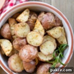 Crispy Roasted Red Potatoes 3 Bowl of chopped roasted and seasoned new potatoes with a red checked towel and a wooden spoon to the side and text Roasted Red Potatoes