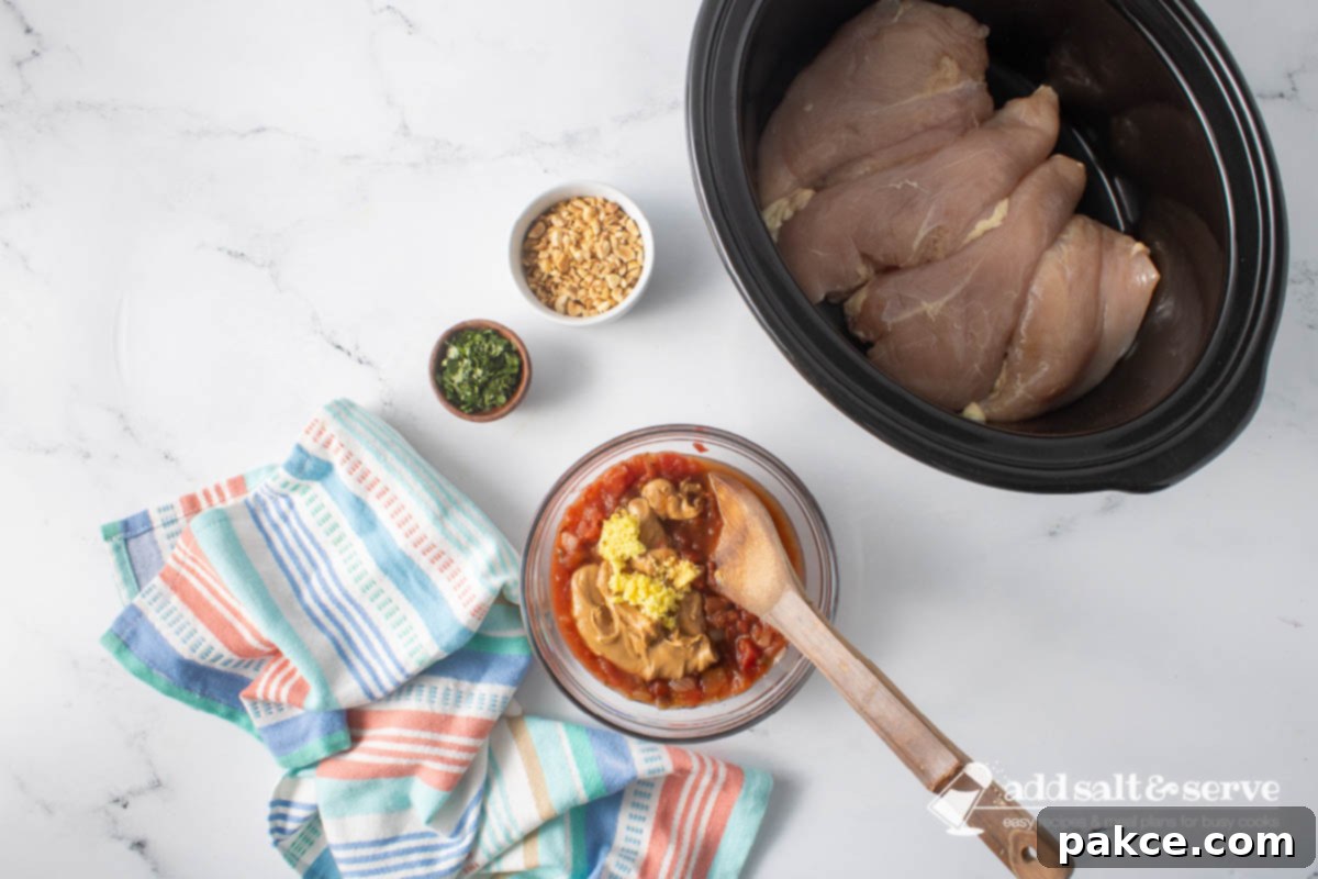 Creamy Slow Cooker Thai Peanut Chicken 5 Uncooked chicken breasts in a slow cooker and small bowls of chopped peanuts and cilantro around a bowl of peanut butter, salsa, soy sauce, grated ginger, and lime juice before mixing.