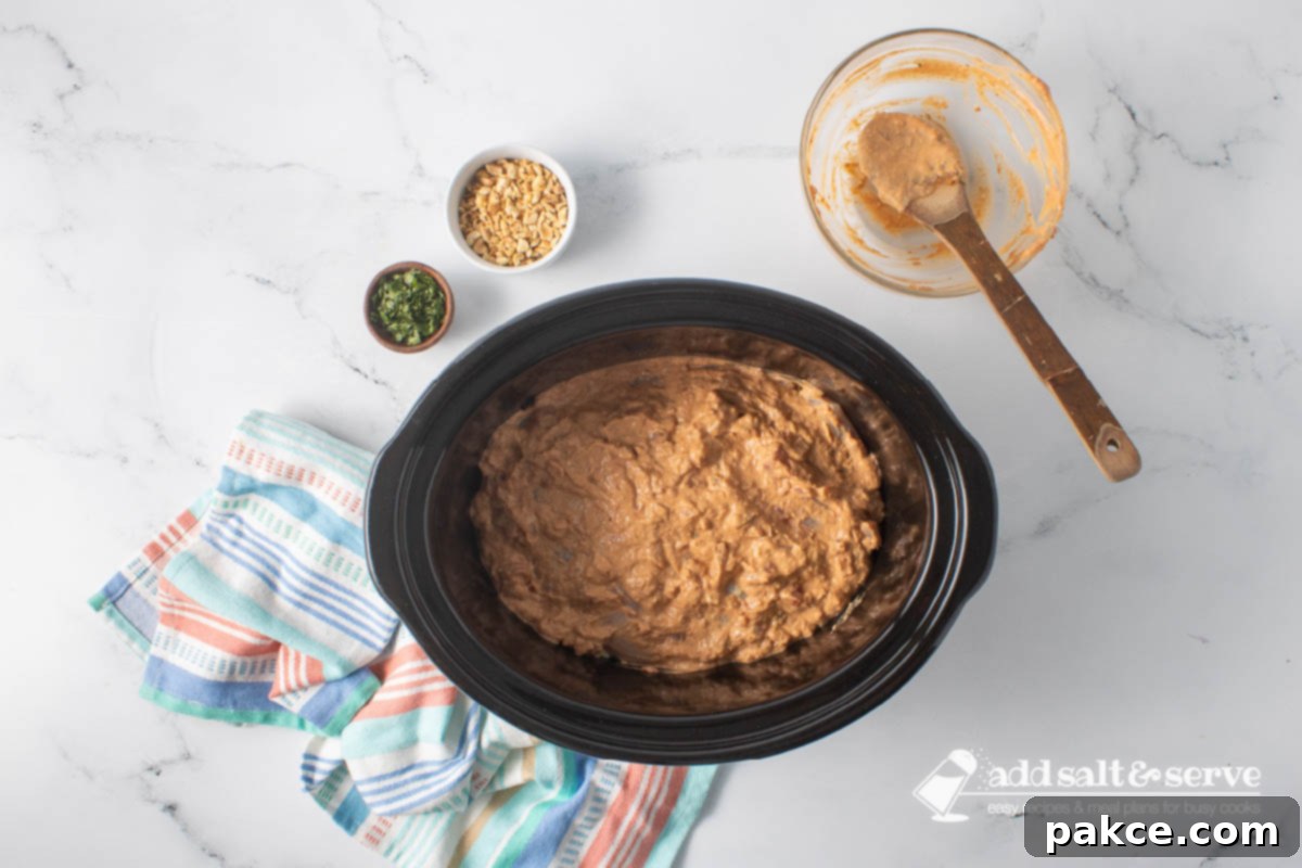 Creamy Slow Cooker Thai Peanut Chicken 6 A slow cooker with chicken covered in a peanut sauce before cooking.