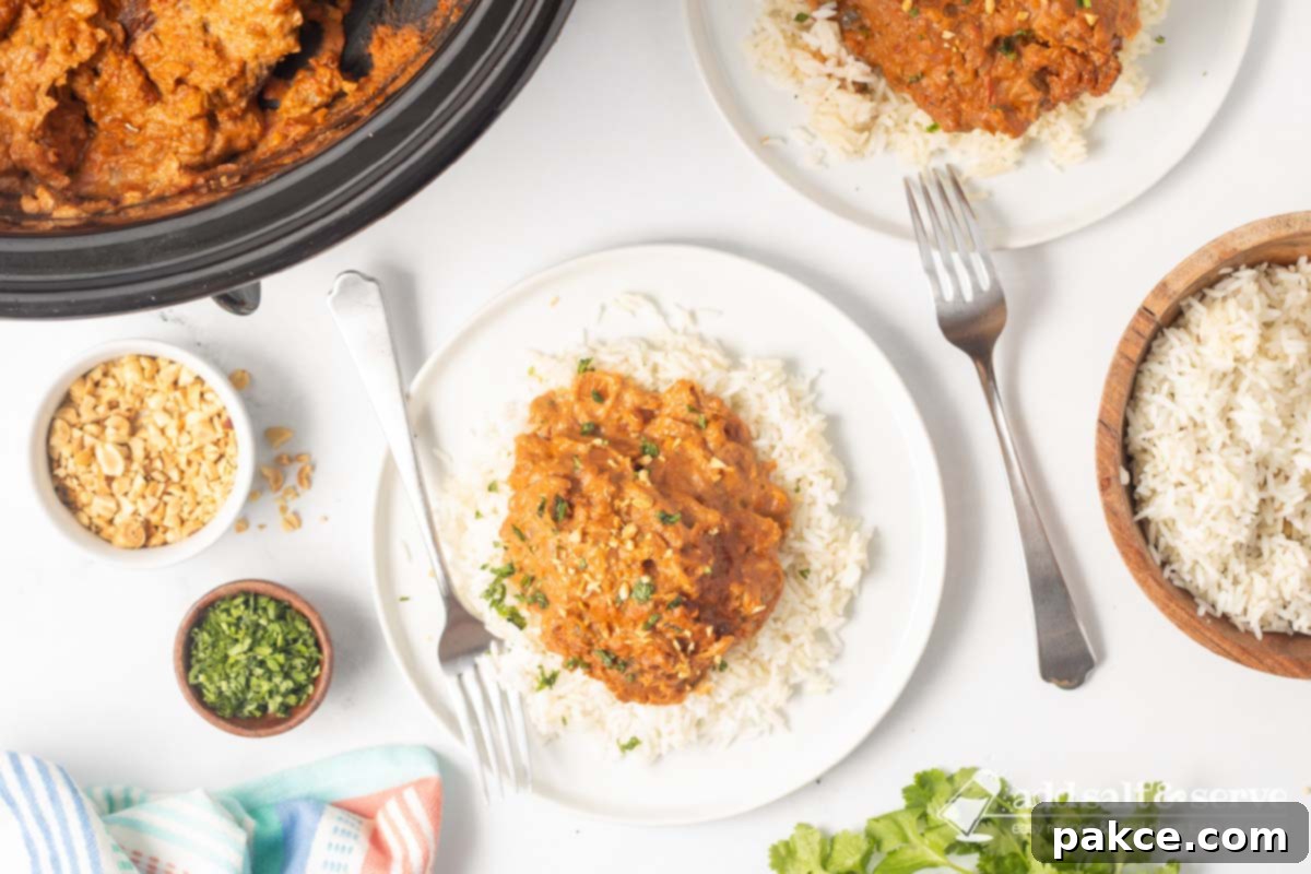 Creamy Slow Cooker Thai Peanut Chicken 8 Plated slow cooker Thai Peanut Chicken over rice garnished with chopped peanuts and cilantro.