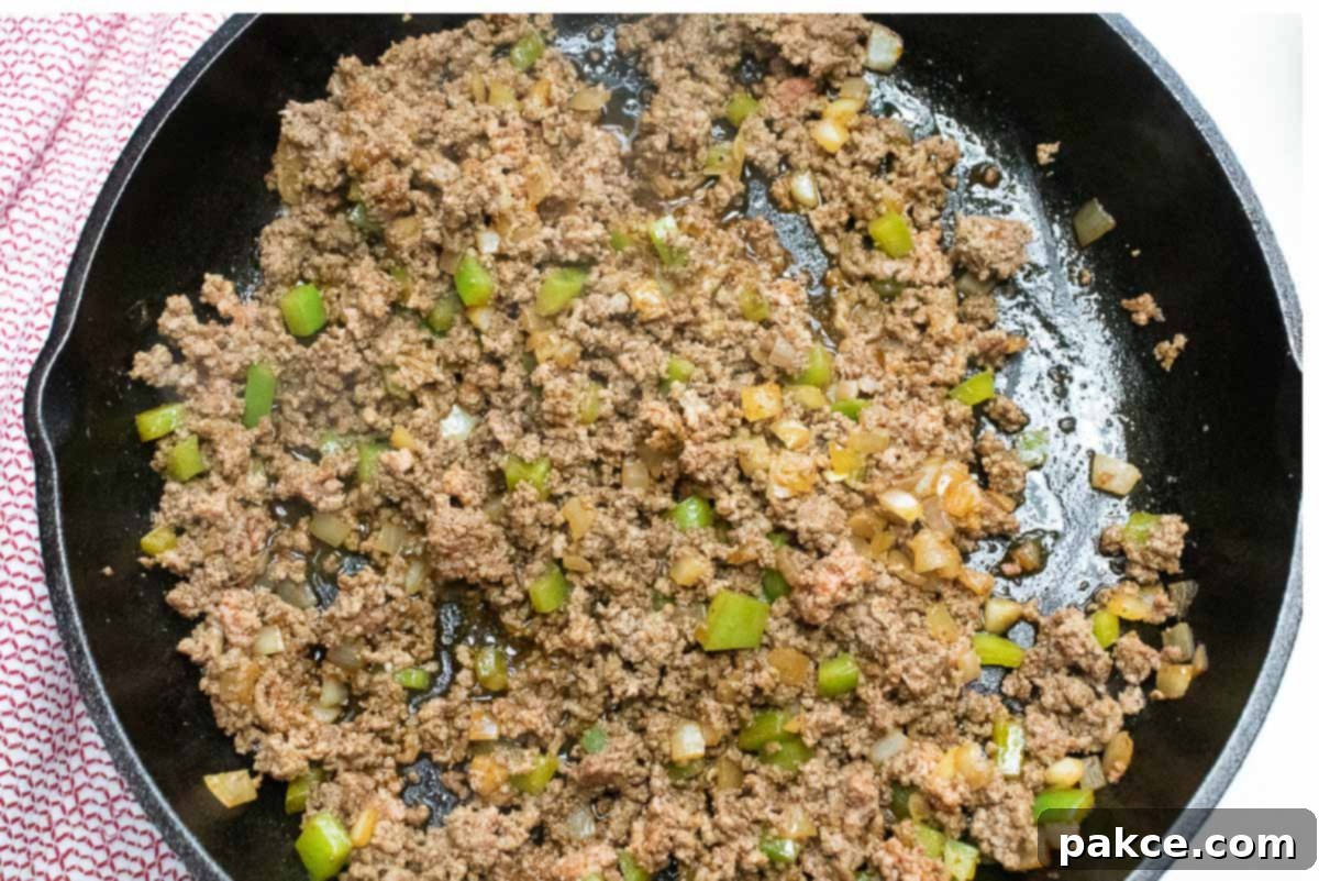 Hearty Cornbread Burger Bake 3 Cooked ground beef, diced onions and bell peppers in a cast iron skillet.