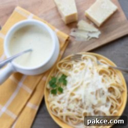 Easy Creamy Homemade Alfredo 2 Overhead shot of yellow plate with fettuccine and Alfredo sauce with pot of Alfredo sauce, hunk of Parmesan cheese, and nutmeg grinder surrounding plate