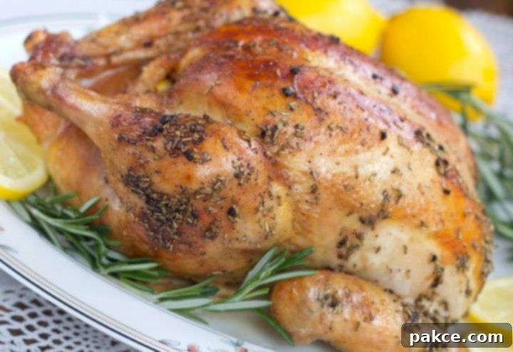 Succulent whole roasted chicken presented on a white plate, elegantly garnished with fresh sprigs of rosemary and bright, thinly sliced lemon.
