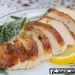 Zesty Lemon and Rosemary Chicken 2 Close-up of succulent slices of roasted chicken, artfully arranged and garnished with vibrant fresh rosemary sprigs and delicate lemon slices on a pristine white plate.