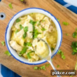 Easy Slow Cooker Chicken and Dumplings with Biscuits 4 Chicken and dumplings garnished with parsley in a white bowl with a blue rim. There is a spoon with a dumpling and some broth. The bowl is on a wooden cutting board on top of a blue napkin with white stripes, all on a white marble counter.