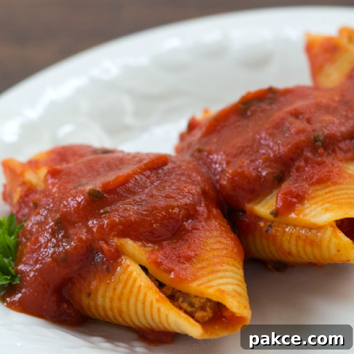 White plate with 3 jumbo pasta shells stuffed with beef and covered with spaghetti sauce, garnished with parsley