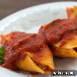 Savory Beef and Spinach Stuffed Shells 3 White plate with 3 jumbo pasta shells stuffed with beef and covered with spaghetti sauce, garnished with parsley
