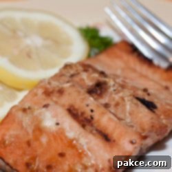 Easy Baked Salmon Teriyaki 2 Pieces of cooked salmon on a white plate with a fork, garnished with two lemon slices and parsley